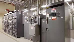Industrial electrical panels and conduit system inside a well-lit utility room with visible caution signage and wiring equipment