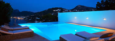 Modern residential pool at dusk with illuminated water, lounge chairs, and clear mountain backdrop